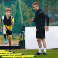 Ladder Drills for Soccer. Group of Young Boys on Football Training With Coach. Young Man as a Sports Trainer Showing to Male Youth Soccer Team how to Exercise on Agility Ladder Ladder Drills for Soccer. Group of Young Boys on Football Training With Coach. Young Man as a Sports Trainer Showing to Male Youth Soccer Team how to Exercise on Agility Ladder