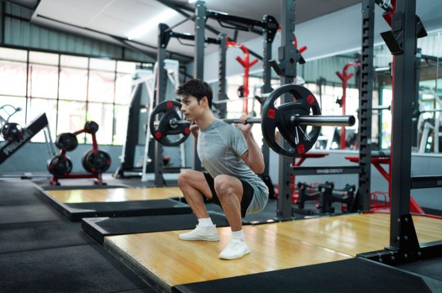 muscular body builder sport man is practice weight training on squat barbell for core muscle inside gym with dark background for exercising and workout usage.