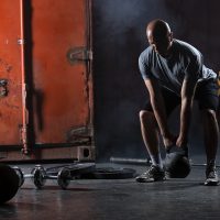 Bald charismatic athlete doing squats with weights. Bald charismatic athlete doing squats with weights. Studio shot in a dark tone.