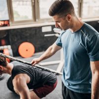 Personal coach helping a man in weightlifting training Two men, personal coach assisting a man in weightlifting training in gym.