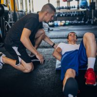 Man exercises with personal trainer Two men, personal trainer assisting a young man in exercises in gym.